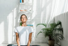 Beautiful Happy Girl With Closed Eyes Practicing Yoga In Lotus Position In Bedroom In The Morning