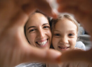 Smiling Hispanic Mom And Biracial Daughter Show Heart Sign